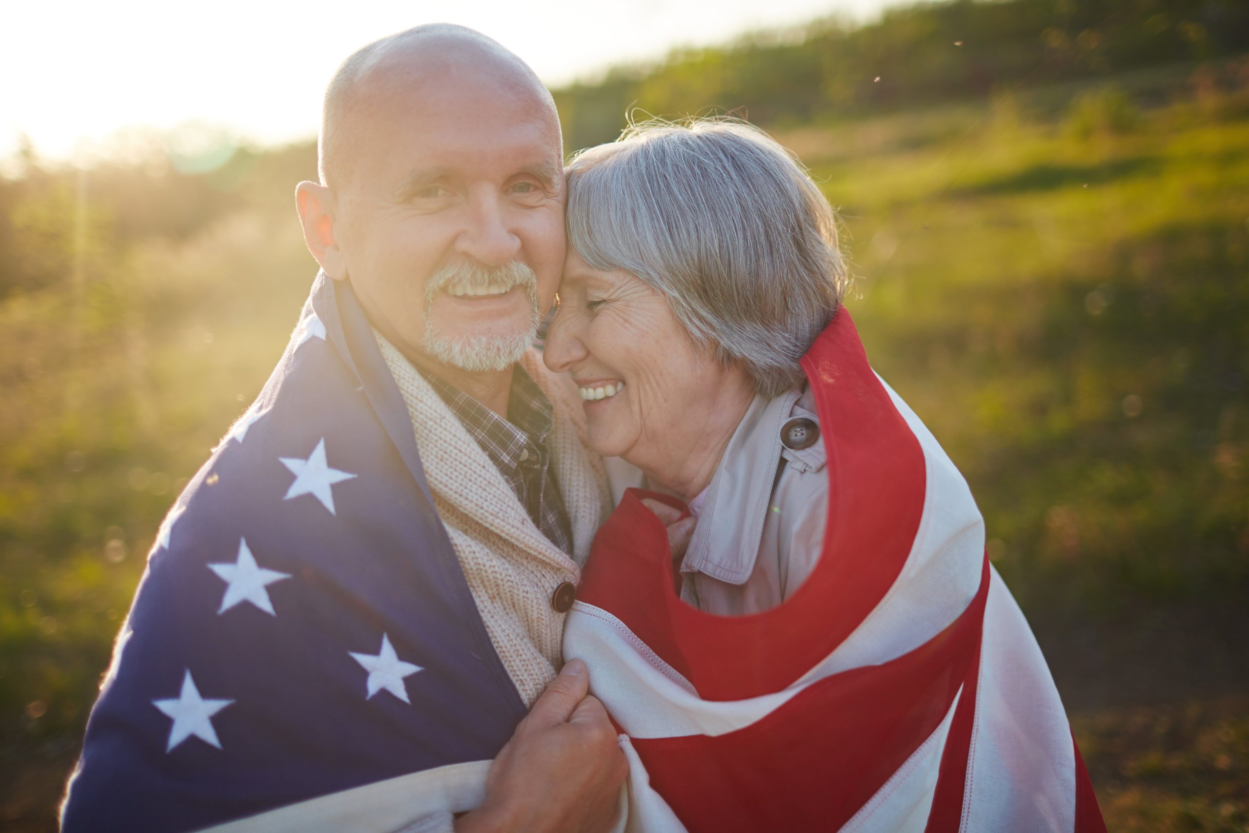 Senior veteran holding USA flag while he hugs his wife.